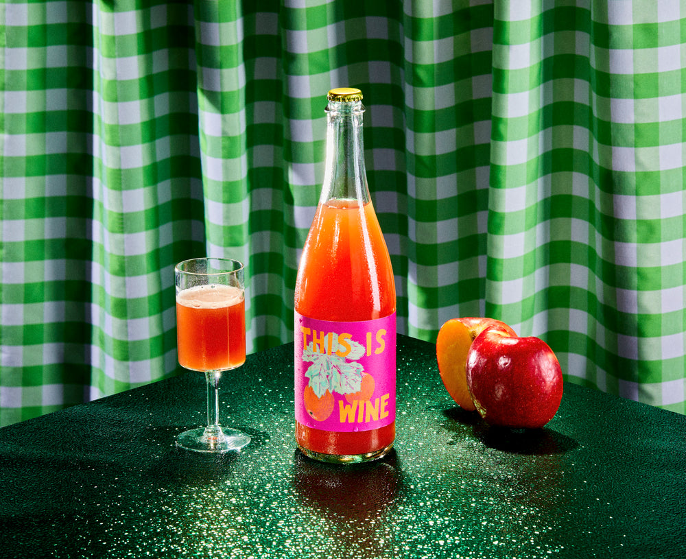 
                  
                    Load image into Gallery viewer, 2021 &amp;#39;This Is Wine&amp;#39; Sparkling Apple Cider Pressed on Carignan Skins with apples and a glass on green chekered background
                  
                